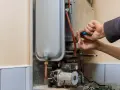 Mani che riparano uno scaldabagno a gas: il bruciatore non parte. Si vede il tecnico con un cacciavite blu.