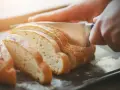 Ręce kroją świeży chleb na kromki. Dowiedz się, jak odświeżyć chleb, by był jak nowy.