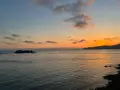 Un tramonto mozzafiato sul mare, con un'isola rocciosa e una barca a vela. Un luogo perfetto per ammirare dove vedere il tramonto a Villasimius.