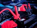 Mechanik w czerwonych rękawiczkach podłącza kable rozruchowe do akumulatora. Czy nowy akumulator trzeba ładować? Sprawdźmy!