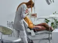 Dentystka w masce i rękawiczkach wykonuje zabieg pacjentowi siedzącemu na fotelu dentystycznym.