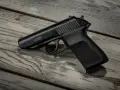 Czarny pistolet P.M.G.-23 leżący na zniszczonej drewnianej desce.