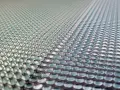 Close-up of a 3d printed lens array, with rows of tiny, clear, dome-shaped lenses reflecting light.