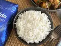 Un tazón de arroz basmati blanco y esponjoso junto a un paquete de Tilda Basmati Original.