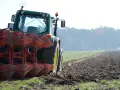 Zielony traktor z pługiem orze pole. W tle mglisty las.
