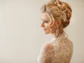 Eleganckie uczesania na wesele średnie włosy: blondynka w koronkowej sukni z perłową ozdobą i długimi kolczykami.