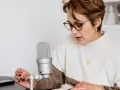 Mujer con gafas lee un libro frente a un micrófono, aprendiendo como escribir mejor.