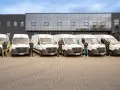 Sześciu mężczyzn w uniformach stoi przed rzędem białych vanów z logo "pharmalink". To zespół odpowiedzialny za transport leków, profesjonalny przewoźnik.