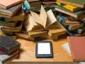 Stosy starych książek i nowoczesny ebook na drewnianym blacie. Wybór między tradycją a technologią.