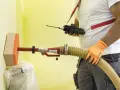 Un técnico usa un dispositivo para insuflar aire a través de una manguera y una esponja en una pared amarilla.