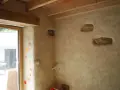 Un mur avec un enduit chaux finition texturé, intégrant des pierres apparentes et des touches de couleur. Le bois des poutres et du cadre de fenêtre apporte de la chaleur.