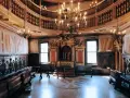 Interno sontuoso della sinagoga di Venezia, con arredi in legno scuro, un grande lampadario e l'Arca Santa dorata.