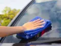 Mano con paño azul limpiando los cristales del coche para una visibilidad perfecta.