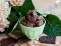 Ein grüner Napf mit zartbitter schokoladeneis, umgeben von Schokoladentafeln, rosa Bonbons und einer Hortensienblüte.