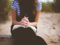 Frau mit verschränkten Händen über einem offenen Buch, die über ihre fertigen Gebete nachdenkt.
