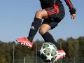 Barn i luften med fotboll. Svarta strumpor med Adidas-logga och benskydd fotboll barn storlek. Orange fotbollsskor med vita detaljer.