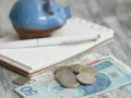 Świnka skarbonka, notatnik i długopis nad polskimi banknotami i monetami. Zastanawiasz się, ile wyniesie waloryzacja kapitału początkowego w 2025?
