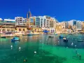 Malta, gdzie na Malcie jest tak pięknie! Woda krystalicznie czysta, łodzie kołyszą się na falach, a w tle kolorowe budynki.