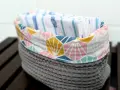 Un panier en tissu gris avec un motif géométrique coloré contient des mouchoirs en tissu. Une idée pour savoir que faire avec des mouchoirs en tissu.