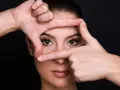 Mani incorniciano il volto di una donna, creando un effetto di profondità. Si può vedere un alone nell'occhio, quasi un riflesso di luce.