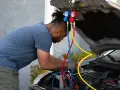 Man working on car engine, using gauges and hoses to fix car AC.