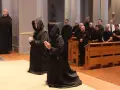 Monk characteristics are evident in the solemn robes and prayerful stances of individuals in a church setting.
