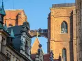 Most zabytkowych budynków we Wrocławiu z ludźmi na moście i wieżą Katedry w tle.