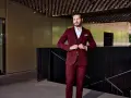 Elegancki mężczyzna w bordowym garniturze i marynarce zapina guziki.