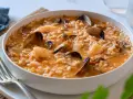Un delicioso arroz caldoso de marisco, repleto de gambas, mejillones y almejas, servido en un cuenco blanco.