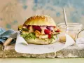 Saftiger halloumi burger mit gegrilltem Gemüse, Rucola und cremiger Sauce auf einem Sesambrötchen.