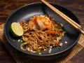 Ein Teller Pad Thai mit Garnelen, Limette und Erdnüssen, bereit zum Genießen.