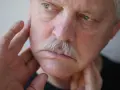 Mann mit Schnurrbart, der sich mit den Fingern das Gesicht berührt, als ob er ein Kribbeln im Gesicht spürt.