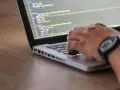 Kodowanie strony internetowej, widać fragment kodu HTML z listą nieuporządkowaną i rękę piszącą na klawiaturze.