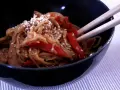 Miseczka pełna aromatycznego makaronu teriyaki z kawałkami kurczaka i papryką, posypana sezamem.