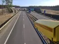 Żółta kamera monitoruje odcinek pomiarowy prędkości na S8. Droga prowadzi przez las, pod wiaduktem.