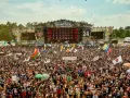 Tłum ludzi na festiwalu Poland Rock, gdzie jest scena i ekrany. Wszędzie flagi i słońce.
