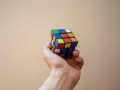 En hand håller en färgglad rubiks kub nyckelring mot en ljus bakgrund.