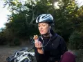 Kobieta w kasku i słuchawkach je ciastko, obok leży rower. To przykład zdrowego odżywiania i aktywnego stylu życia, czyli zbilansowana dieta.