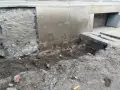 Prace przy wzmocnieniu fundamentów w starym domu. Widoczne wykopy, odsłonięta ściana i nowe elementy betonowe.