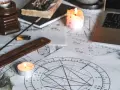 Na stole leżą wykresy astrologiczne, świece, kadzidełko i laptop. Widać symbolikę wskazującą na ascendent w bliźniętach.