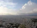 Rozległa panorama Aten z wzgórza Lycabettus. Miasto rozciąga się aż po horyzont, a nad nim piętrzą się chmury.