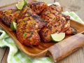 Soczysty filet z kurczaka na grilla, z przypieczonymi paskami i świeżą kolendrą, podany z ćwiartkami limonki na drewnianej tacy.