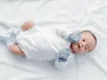 Malutki noworodek nie może zrobić kupy, leży na białym kocyku w niebieskich skarpetkach i rękawiczkach.