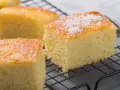 Puszyste ciasto na kefirze, pokrojone w kostkę, z posypką z wiórków kokosowych, prezentuje się apetycznie na kratce.