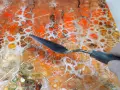 Maintenant, peut-on mettre de la résine sur de la peinture acrylique ? Un outil est utilisé pour travailler une peinture abstraite aux couleurs vives, orange et blanc.