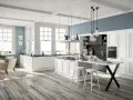 Cucina luminosa con isola centrale, sgabelli bianchi e una nicchia sotto finestra con vista mare.