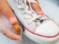 Ręka z gąbką i szczotką czyści białe trampki, usuwając żółte plamy.