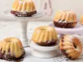 Mehrere mini Gugelhupf mit Puderzucker bestäubt, auf verschiedenen Etageren arrangiert.