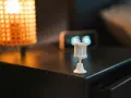 Sensor de movimiento blanco sobre mesita de noche, junto a lámpara y reloj. Ideal para saber como dejar fijo un sensor de movimiento.