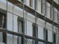Budowa domu z bloczków styropianowych. Rusztowania otaczają białą ścianę z otworami okiennymi i drzwiami, czekającymi na wykończenie.